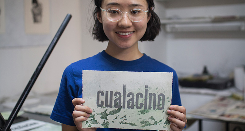 student holding a paper with cualacino print