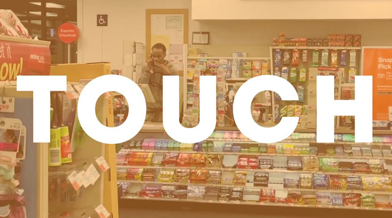 A photo of a man in a food store. On the photo is the white text: Touch.