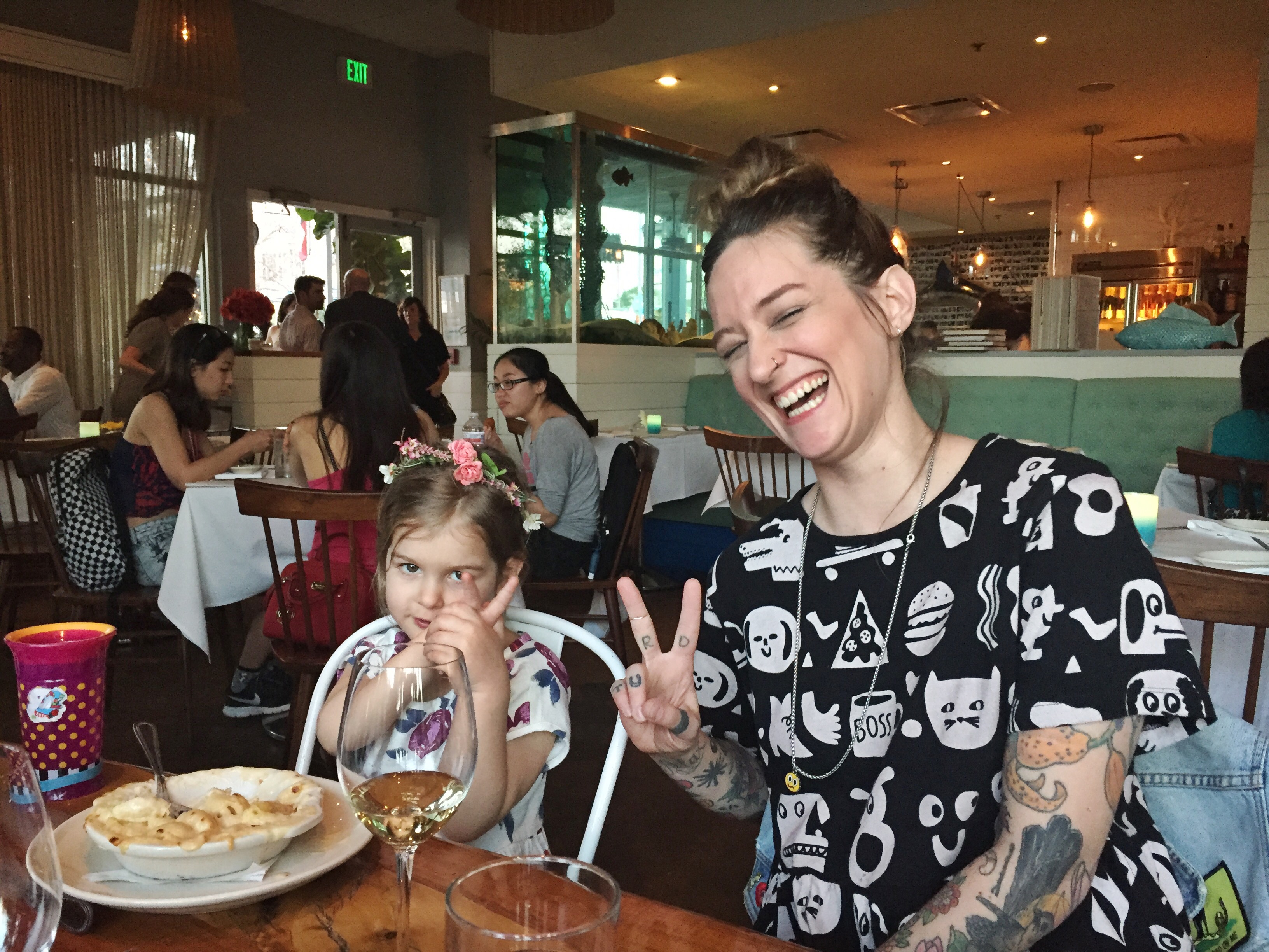 a mom and her daughter sitting at a table showing peace signs with their hands