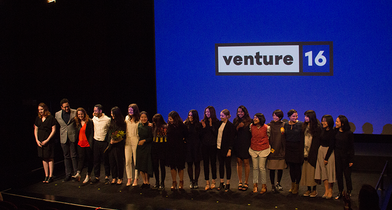 group photo of students on the stage in the venture 16 event with the event logo projected on the screen behind them
