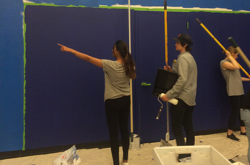 three persons are working on the exhibition gallery installation, and one is painting the wall in blue