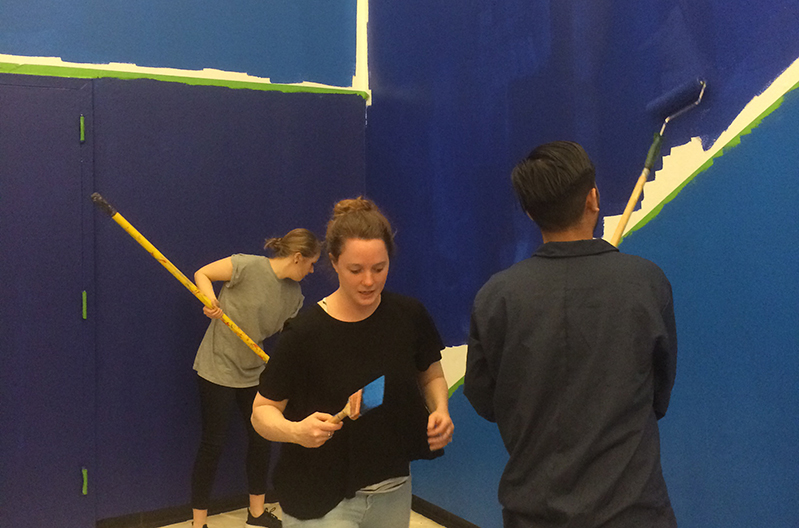 three persons working on painting a wall in blue