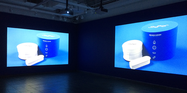 two images projected on two walls of a white product next to its rounded blue box