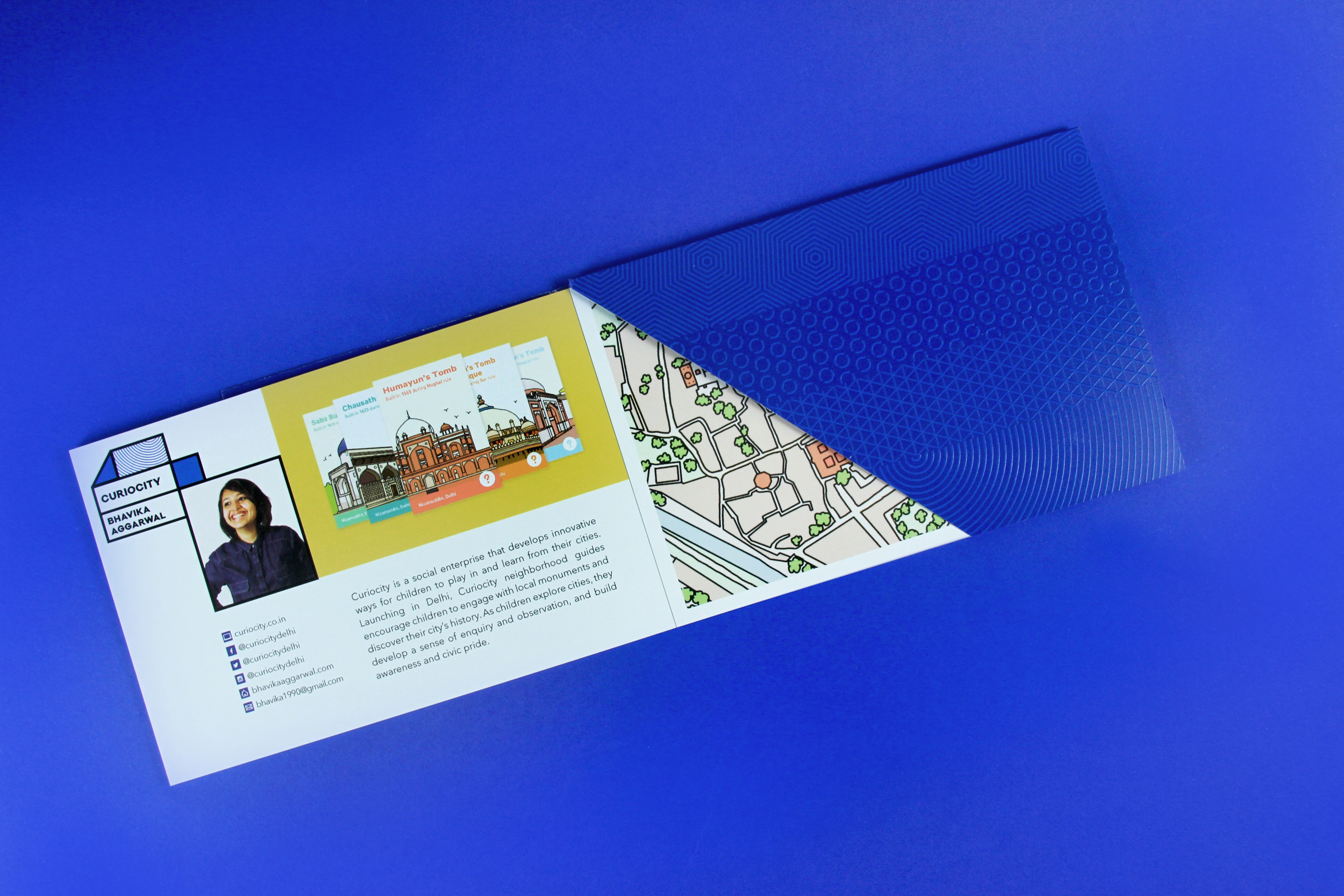 An image of a folded flyer in a blue envelope. On the flyer there is a picture of an Indian woman, the text curiocity, some Indian building drawings and a map of a city.