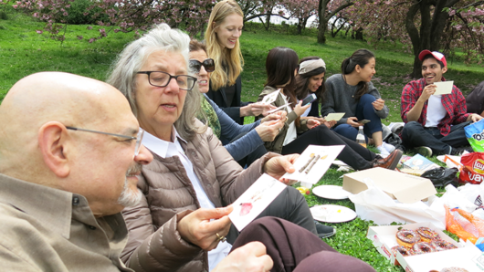 A photo of a group of people checking some post cards, while having a picnic.