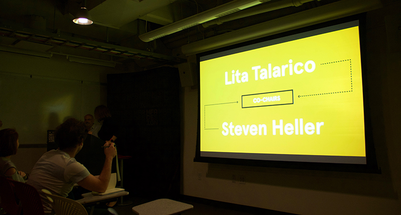 A photo of a screen projector showing a yellow image with some white text that says: Lita Talarico, Steven Heller.