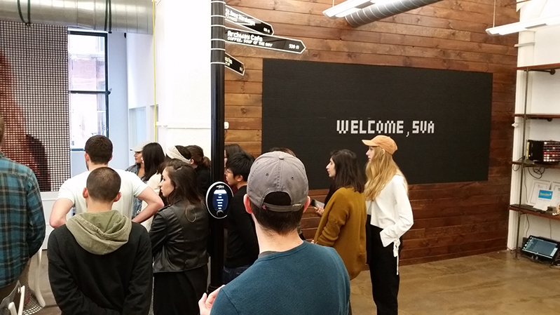 A photo of a group of students standing in an exhibition room. On the wall there is a board with text: Welcome SVA.