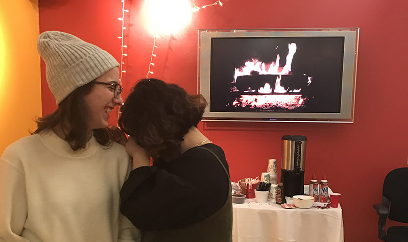 two girls having and laughing in a room with a red wall and a tv screen with a scene of a fireplace on it