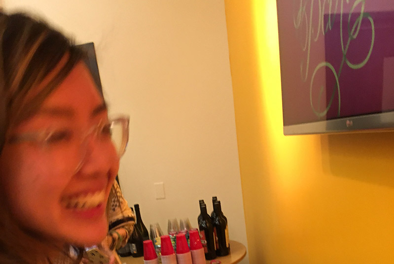 snapshot of a woman's face and a part of a tv screen and a table with wine and glasses in the background