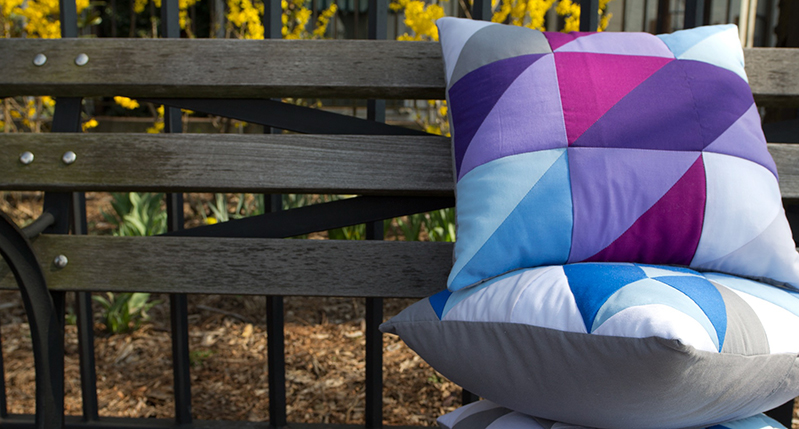 A photo of some colorful pillows put on a bench in the park.
