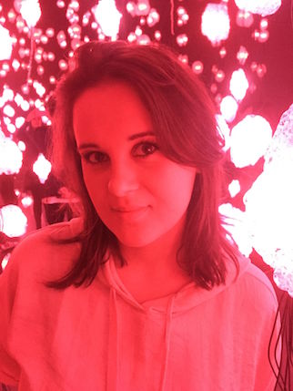 A red colored photo of a woman wearing a hoodie, standing in front of some bright lights.
