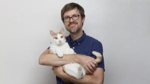 bearded man in blue shirt with a large white cat