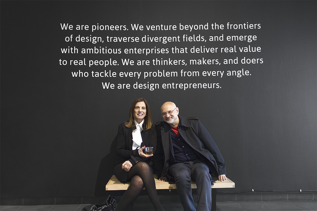 A photo of two teachers sitting on a bench. Also behind them on a wall there is a text: We are pioneers. We venture beyond the frontiers of design, travers divergent fields, and emerge with ambitious enterprises that deliver real value to real people. We are thinkers, makers, and doers who tackle every problem from every angle. We are design entrepreneurs.