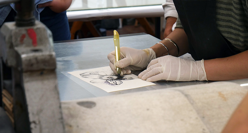 Student wearing white gloves and meticulously working on a flower design on paper.