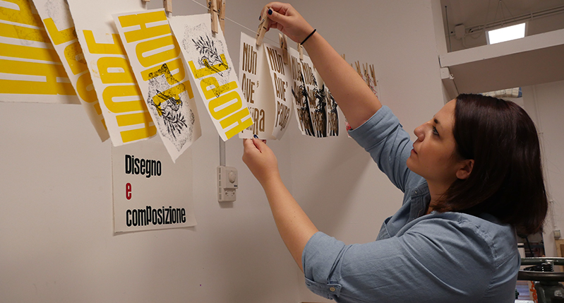 Student hanging some fresh pressed posters to dry on a wire.
