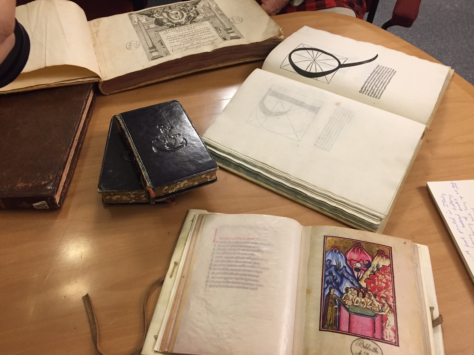 Old books depicting letter calligraphy and colorful hand drawings. There are some old, cover embossed notebooks on the desk as well.