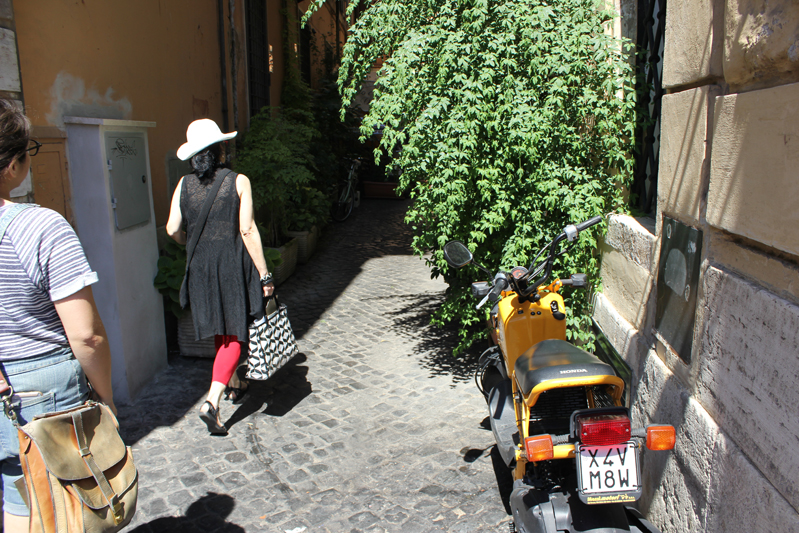 photo of people walking on the sidewalk and a yellow scooter near a wall