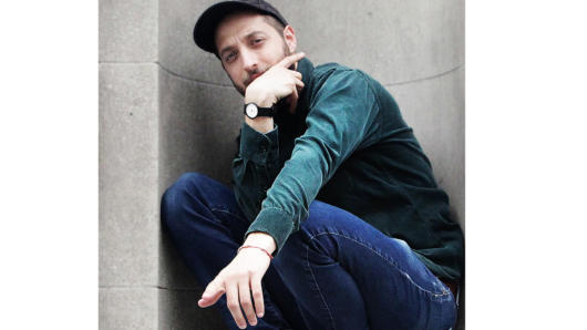 A man with a watch and cap, near a wall thinking and pointing a finger.