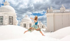 A photo of a girl wearing a colorful dress, running on some white roof tops in the sun light.