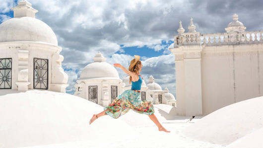 A photo of a girl wearing a colorful dress, running on some white roof tops in the sun light.
