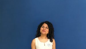 A photo of a woman wearing a white dress and standing in front of a blue screen.