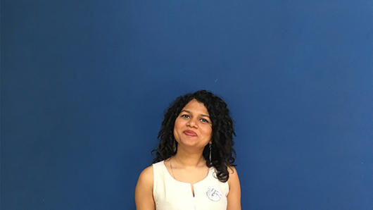 A photo of a woman wearing a white dress and standing in front of a blue screen.