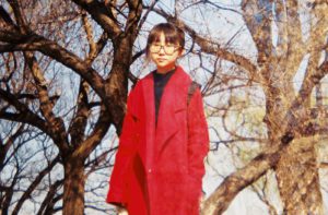 A girl with galssess dressed in a red coat and in the background some trees