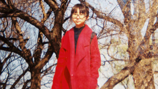 A girl with galssess dressed in a red coat and in the background some trees