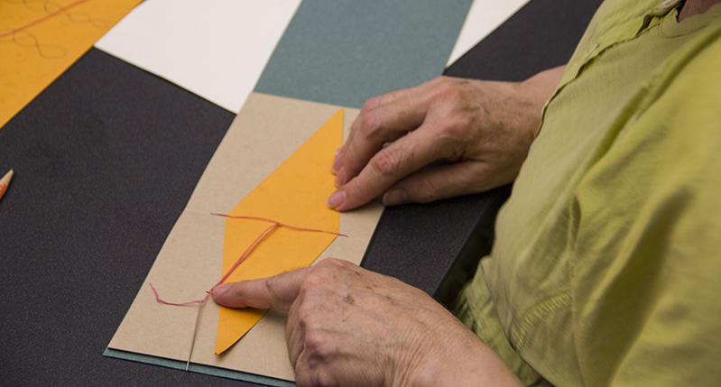 A person working with some colored paper, a needle and a piece of wire.