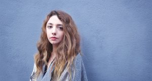 A photo of a girl sitting in front of a blue wall.