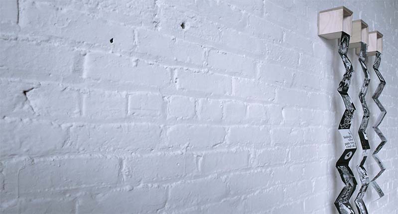 A photo of a white brick wall and on it there are some wood boxes with some zig zag paper flyers popping from them.