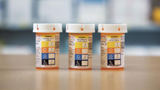 A photo of three identical pill bottles, each with a label depicting four colors and icons. Each color and icon represents a part of a day and on the other side how many pills must be taken. There is yellow with a sun representing morning, orange with the sun representing evening, blue with half of sun representing afternoon and black with a moon representing midnight.