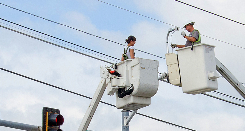 A photo of some workers standing in some lift buckets and working on electrical power lines.