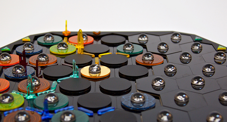 A photo of a black glass board, some hexagon tiles, some marbles and some colorful glass structures on it.