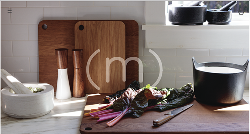A photo of a kitchen's table, filled with different tool and some vegetables on which a few rays of sunlight shine trough a window.