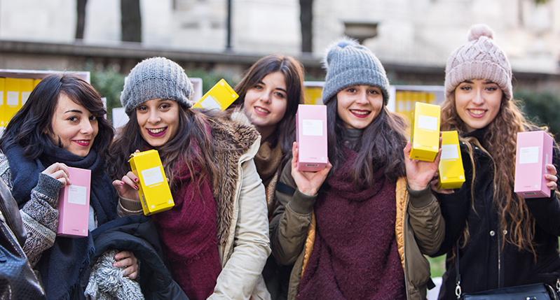 A photo of a group of smiling girls holding pink and yellow boxes in their hands.