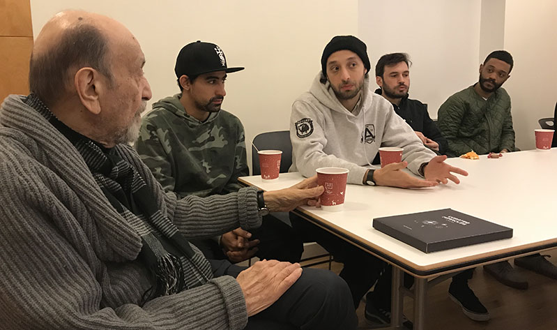 A photo of a group of students and a teacher sitting at a table and drinking coffee.