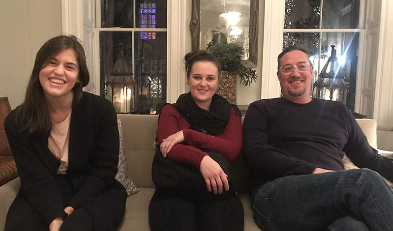 A photo of three persons sitting on a couch in a room.