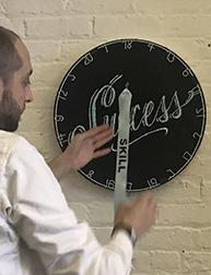 A photo of a person dressed in white and working on some sort of disk object with numbers and the text Success on it. Also on the disk there is a ribbon with the text Skill on it.