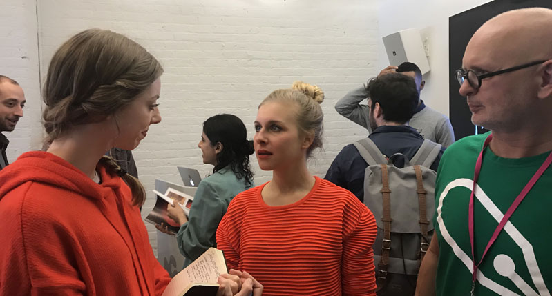A photo of three people talking while holding some books and standing in a crowded room.