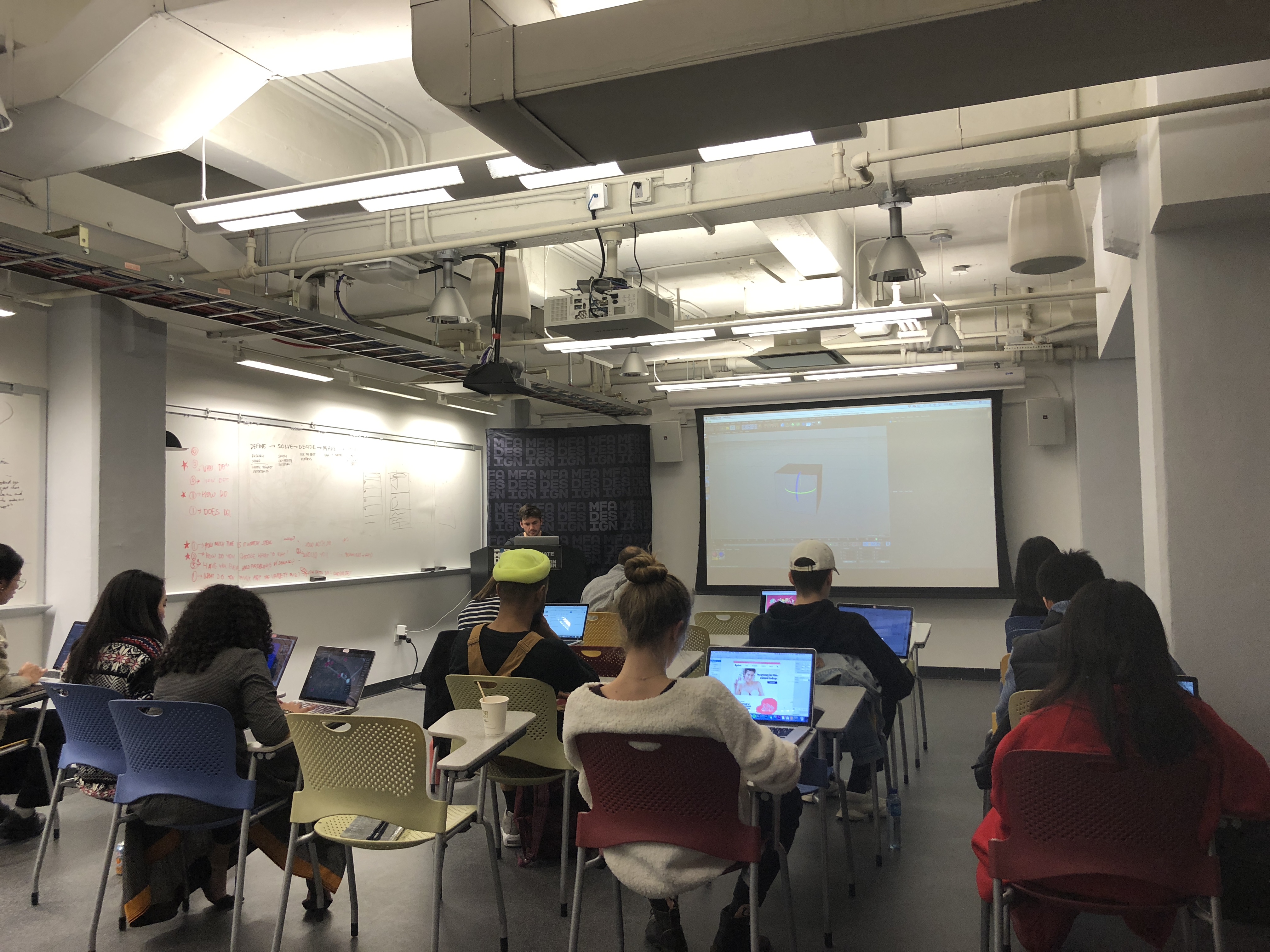 A photo from a classroom showing students sitting at their desks and following a lecture on a screen projector.
