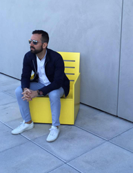 A photo of a man wearing sunglasses and sitting on a yellow wooden chair.