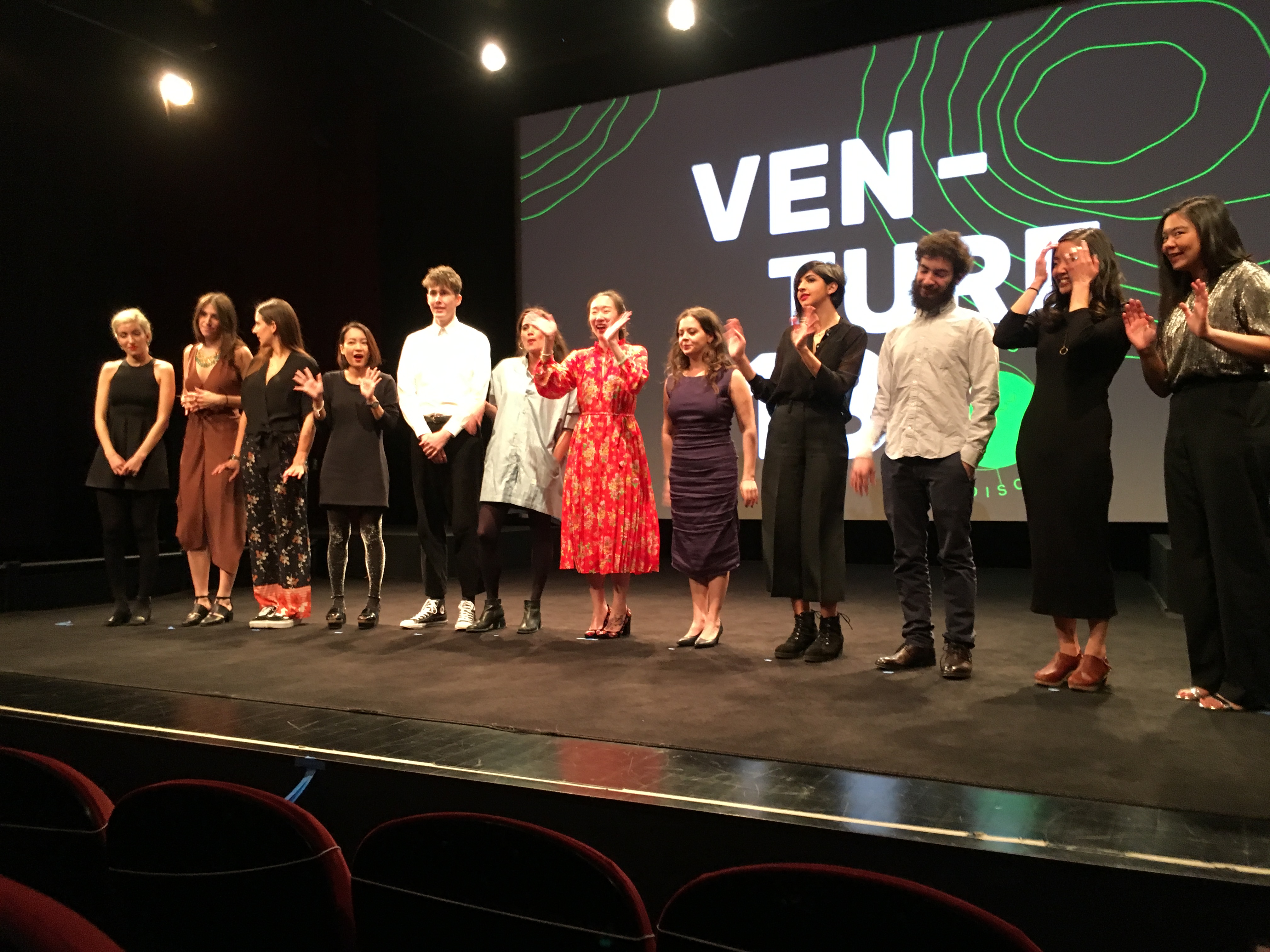 A photo of a group of people sitting on a stage in front of a screen projector that has some green lines and the text Venture.