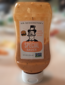 A plastic bottle filled with some orange looking sauce and on it a label with a drawing of a man with a hat and a monocle. On the label there is the text: Special Sauce.