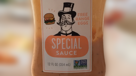A plastic bottle filled with some orange looking sauce and on it a label with a drawing of a man with a hat and a monocle. On the label there is the text: Special Sauce.