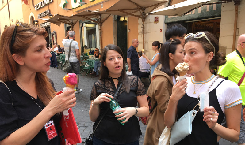 A photo of three women enjoying some ice-cream while sitting in the street.