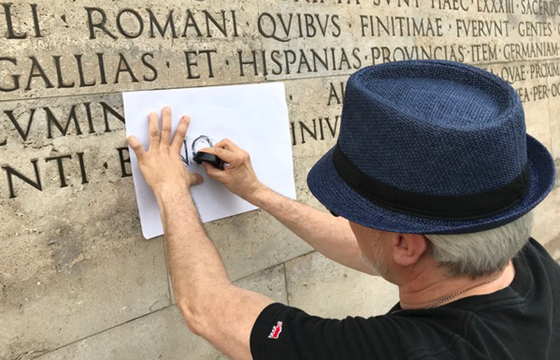 A photo of a man copying some Latin carvings on a piece of paper.