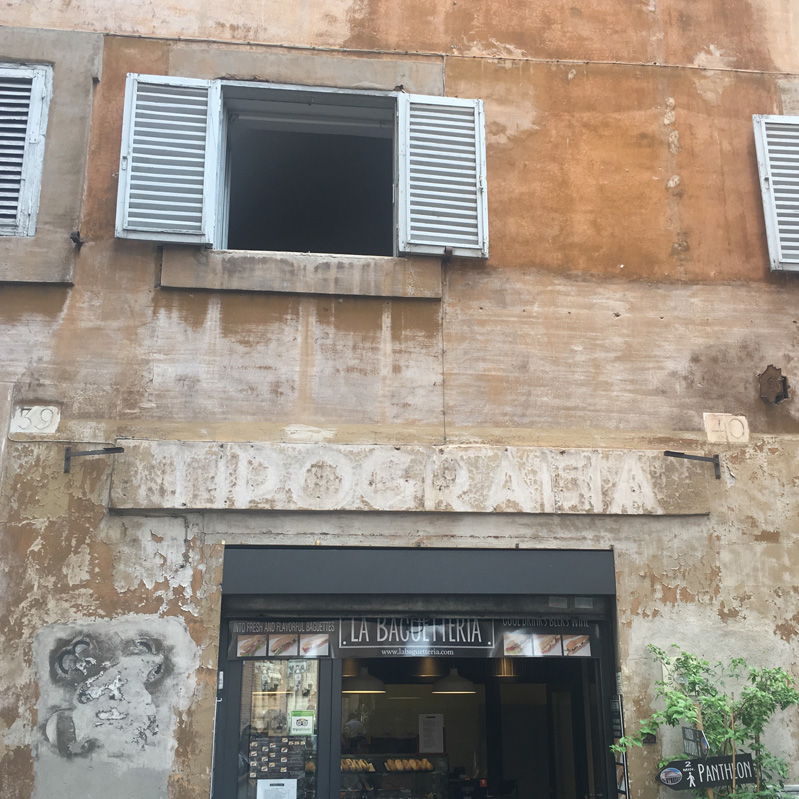 A photo of a shop entrance with a faded stone text: TIPOGRAFIA.