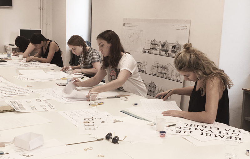 A photo of a group of students working at a table, trying to draw letters for the typography course.