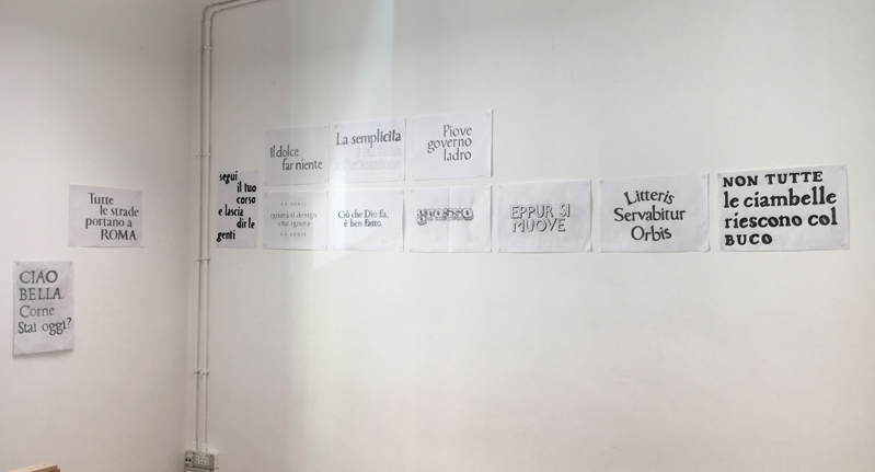 A photo of some sample papers glued on the wall. Each paper has some typographical letters drawn by students in multiple styles.